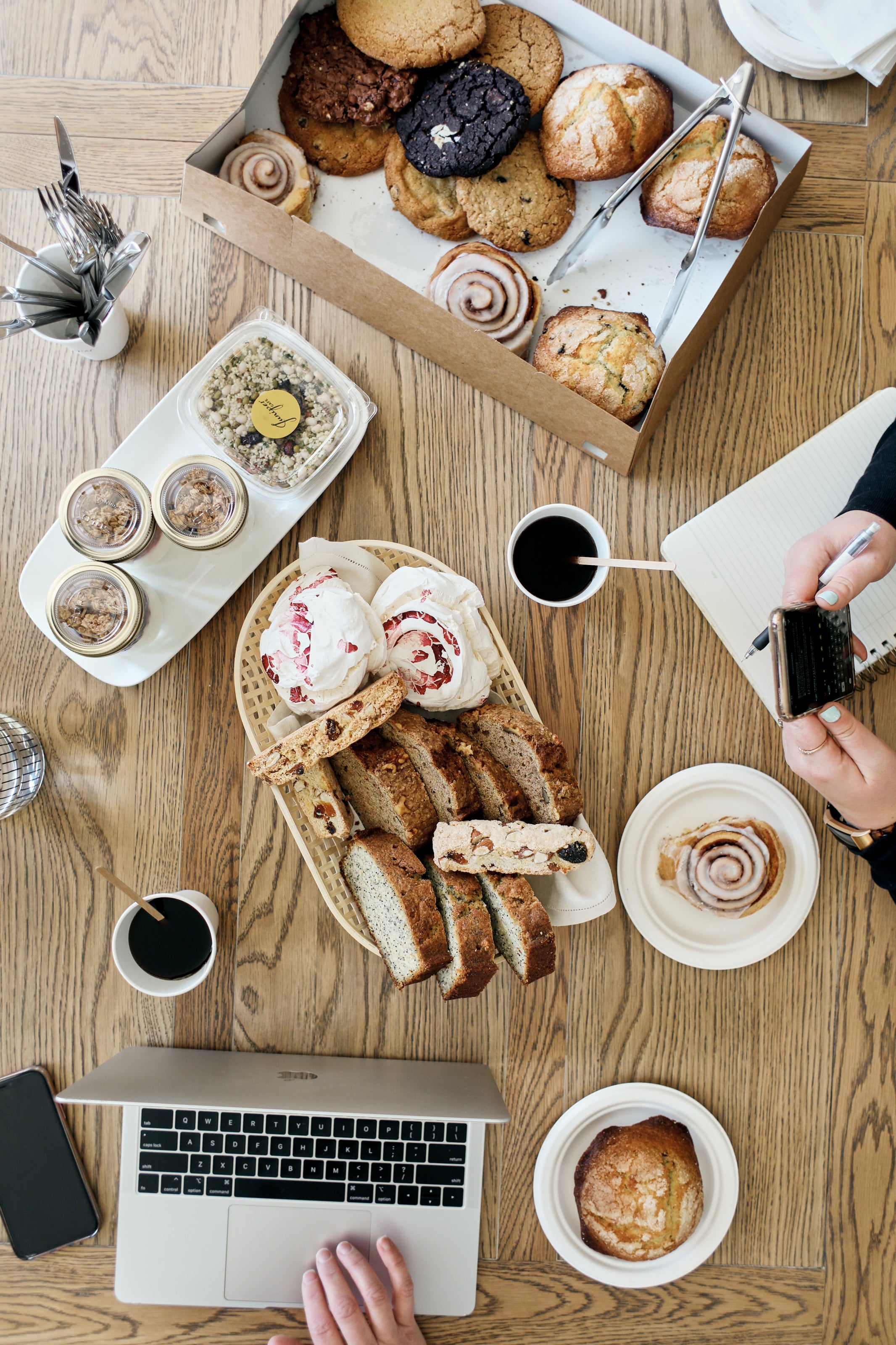 An image showing food catered to a work station, including finger food that is easy to eat such as bread, cookies and cinnamon rolls.